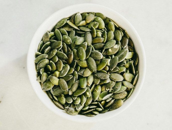 Top view of a white bowl of pumpkin seeds