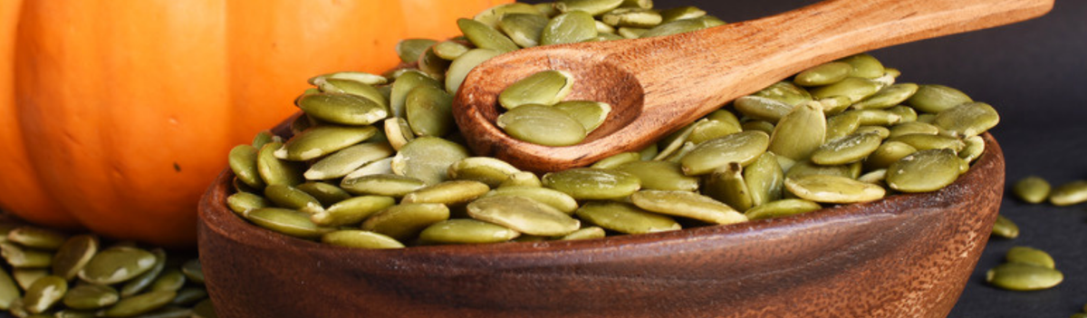 Wooden bowl and spoon of pumpkin seeds beside a small pumpkin