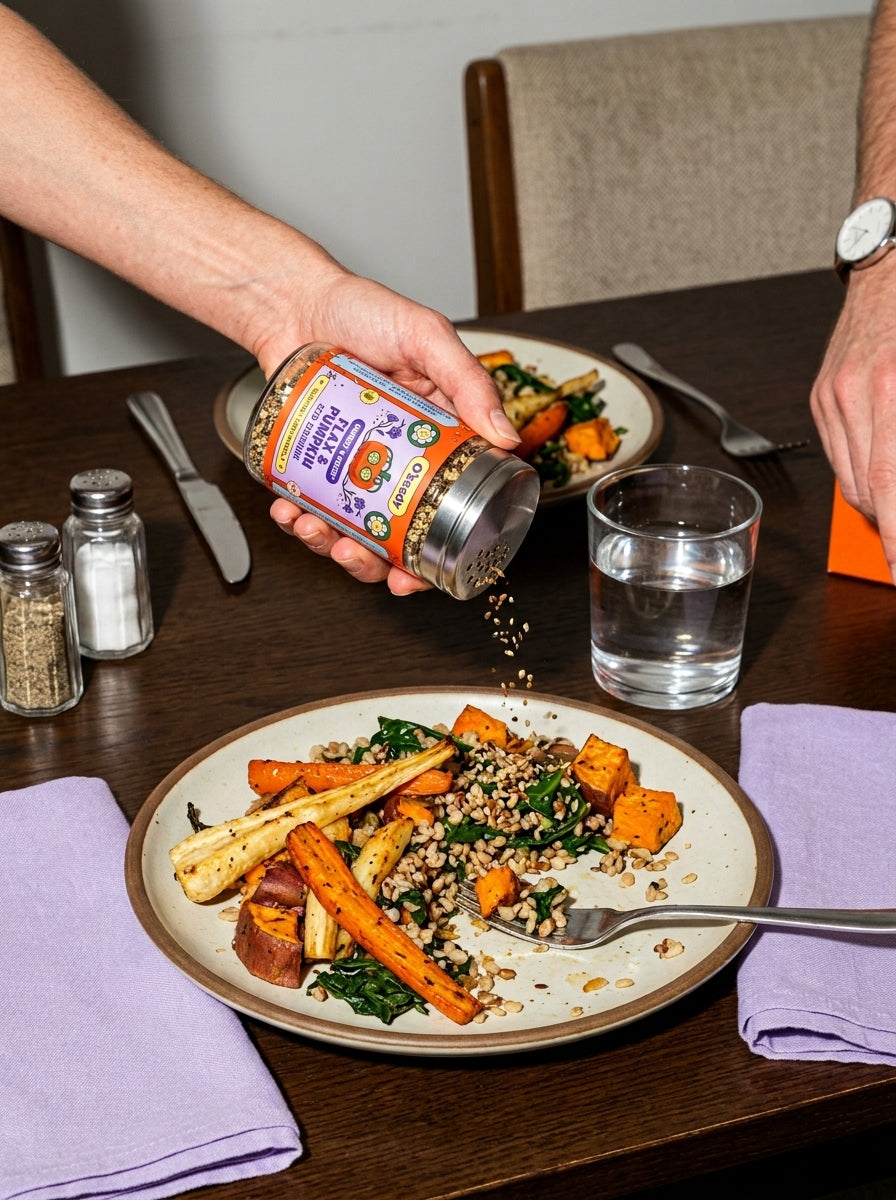 A hand shaking OSEEDY over roasted vegetables and grains at an everyday dining table